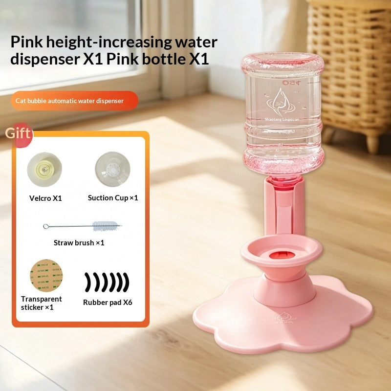 Pink automatic cat water dispenser with a clear bottle, shown on a wooden floor with an inset product kit list. The kit includes a pink dispenser, a clear bottle, a Velcro hook, a suction cup, a cleaning brush, a straw, and transparent stickers.