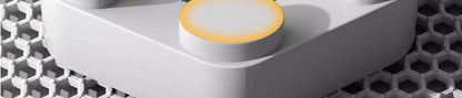 Close-up of a white electronic device with a yellow button on a honeycomb background
