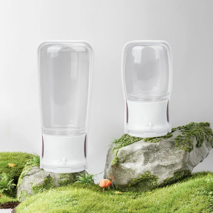 Two clear glass tumblers on a rock with grass and flowers in the background
