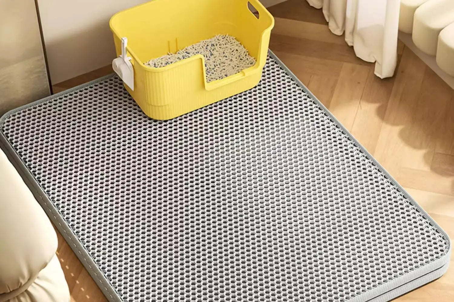 Gray perforated mat with a yellow litter box on a wooden floor.